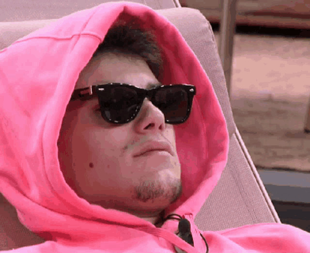 a man wearing sunglasses and a pink hoodie is laying down