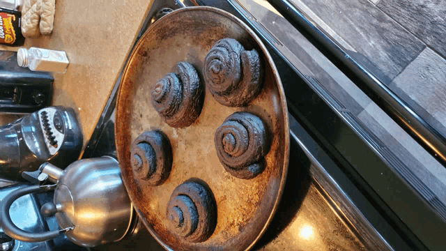 a bunch of cinnamon rolls are on a pan on a stove top with a bottle of doughnuts in the background