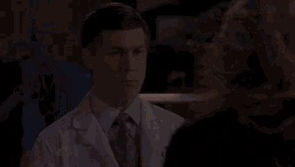 a man in a lab coat and tie is talking to a woman in a courtroom .