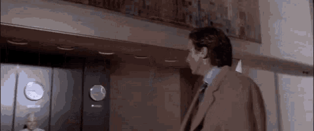 a man in a suit and tie is standing in front of a clock in a room .