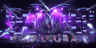 a group of people are dancing on a stage with purple and blue lights
