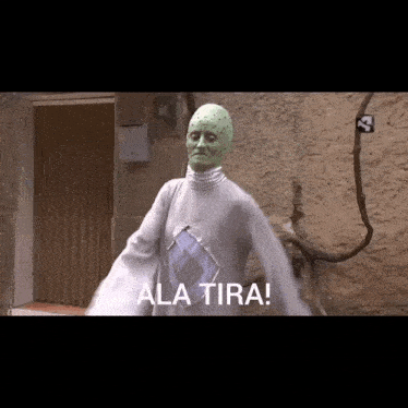 a man with a green face is standing in front of a wall with the words ala tira written below him