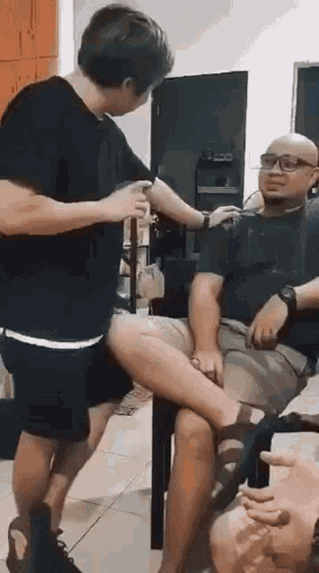 two men are standing next to each other in a room while a man sits on a table .