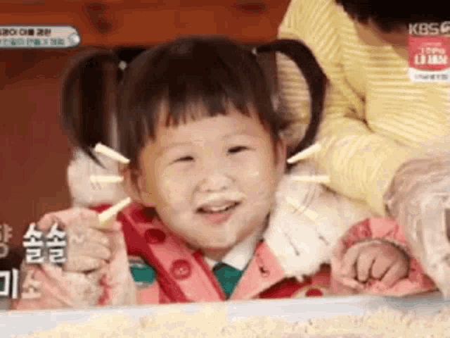 a little girl with pigtails is smiling for the camera while a woman holds her arm around her shoulder .
