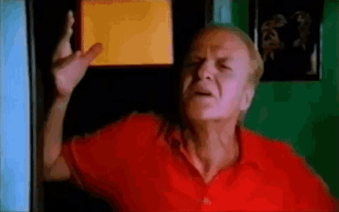 a man in a red shirt is standing in front of a door and making a funny face .