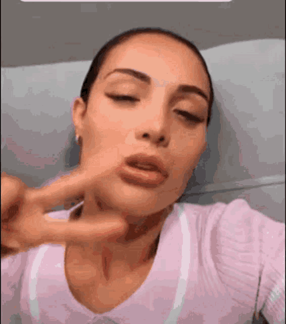 a woman in a pink sweater is making a peace sign with her finger .