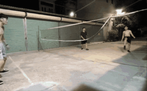 a group of men are playing volleyball on a concrete court at night