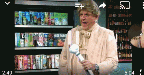 a man in a white suit is holding a remote control in front of a shelf full of dvds including one titled movie