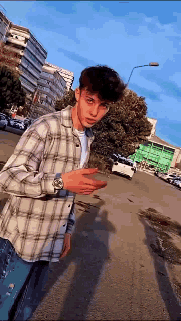 a young man wearing a plaid shirt and a watch is standing on the side of the road .