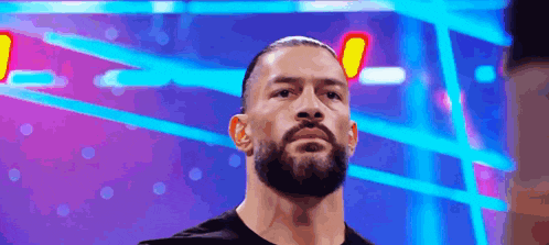 a man with a beard and a black shirt is standing in front of a blue and purple background .