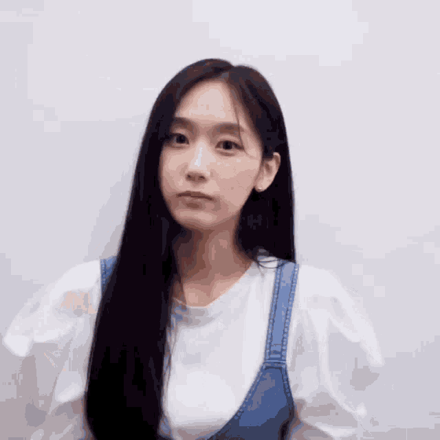 a woman with long black hair wearing a white shirt and overalls