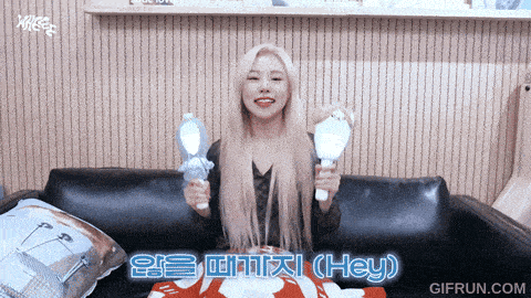 a woman is sitting on a couch holding two light sticks and says hey in a foreign language