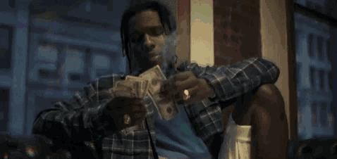 a man is smoking a cigarette and holding a pile of money .