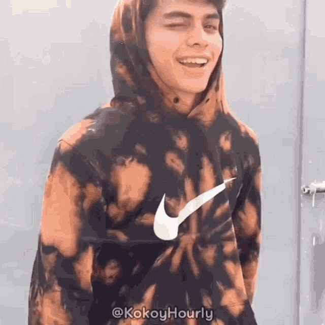 a man wearing a tie dye nike hoodie is smiling .
