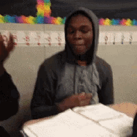 a man in a hoodie is sitting at a desk with a book