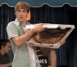 a man is holding a large pizza in a box and says bones .