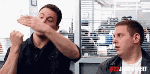 two men are sitting next to each other in an office and one of them is doing a dab .