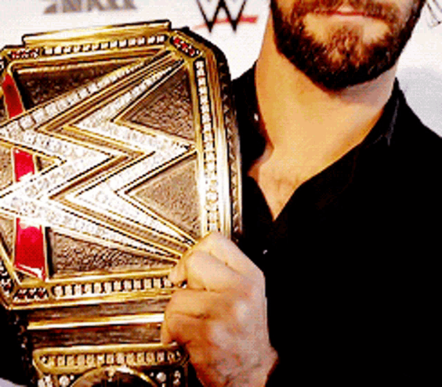 a man with a beard is holding a gold wrestling championship belt