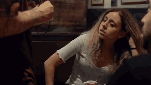 a woman is sitting at a table with a cup of coffee and a man is holding her hair .