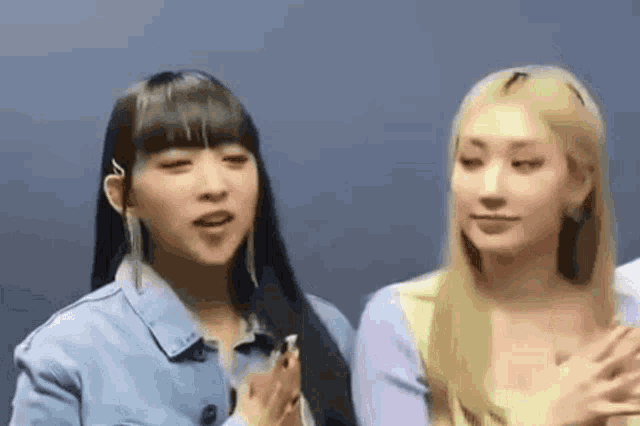 two women are standing next to each other with their hands on their hearts .