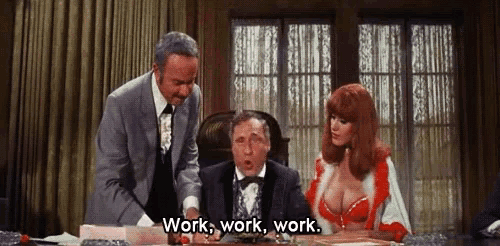 a man in a tuxedo is sitting at a desk with a woman in a red dress saying work work work