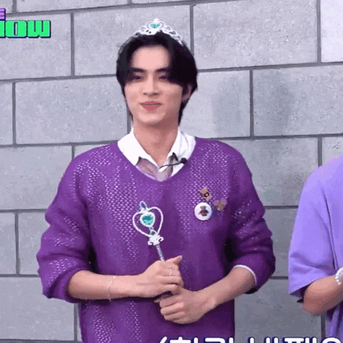 a man wearing a purple sweater and a tiara holds a wand in his hand
