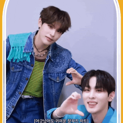 two young men are making a heart shape with their hands and one of them is wearing a blue jacket
