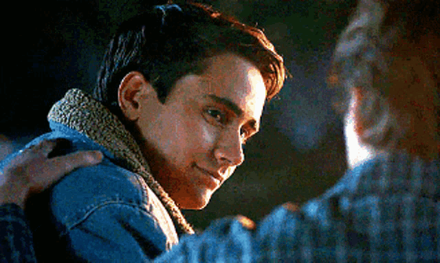 a young man in a denim jacket is being hugged by a man in a plaid shirt .
