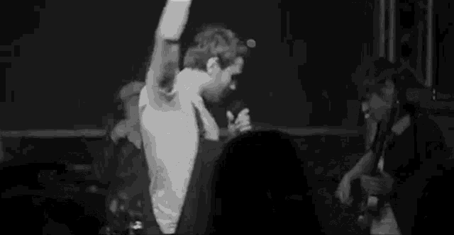 a man is dancing on stage in front of a crowd while a man plays a guitar .