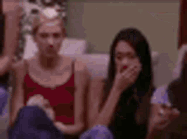a group of women are sitting on a couch and one of them is covering her mouth .