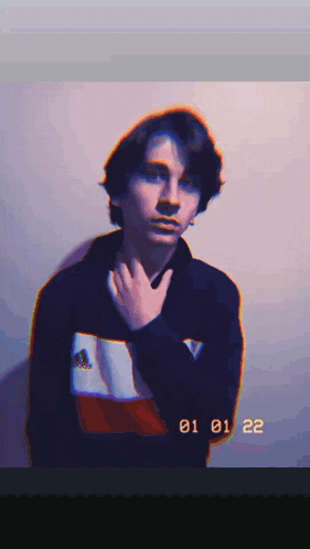 a young man in a black adidas sweatshirt holds his hand to his chin