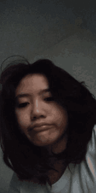 a young woman with long black hair is making a funny face while wearing a white shirt .