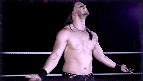 a shirtless wrestler with his arms outstretched stands in a ring