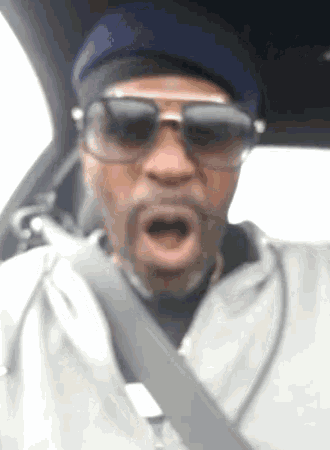 a man wearing sunglasses and a beanie is driving a car