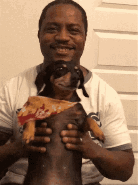a man is holding a puppy with a slice of pizza on its back