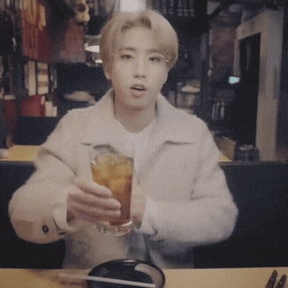 a young man is sitting at a table holding a drink