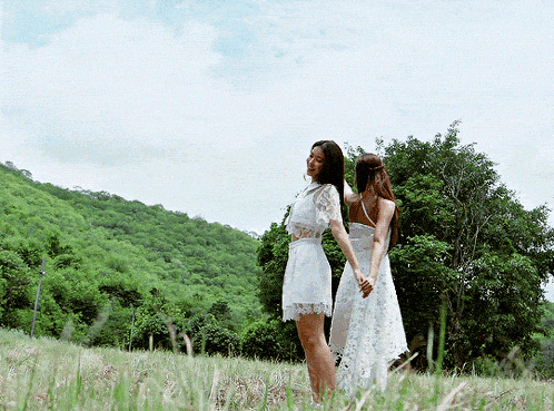 two women in white dresses are standing in a grassy field
