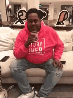 a man in a pink hoodie is sitting on a couch drinking a glass of wine .