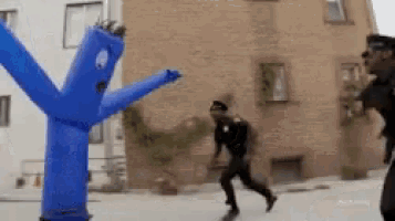 a man in a police uniform is running in front of a blue inflatable man