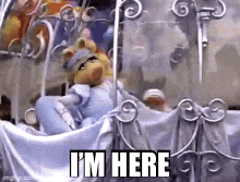 miss piggy is sitting in a stroller with the words `` i 'm here '' written above her .