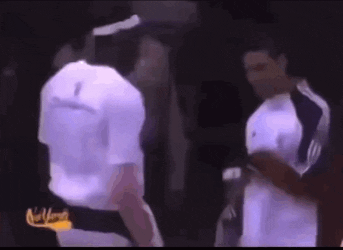 two men are standing next to each other and shaking hands in a dark room .