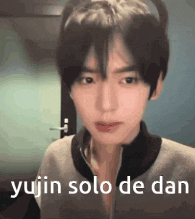 a young man is standing in front of a door with the words `` yujin solo de dan '' written on his face .