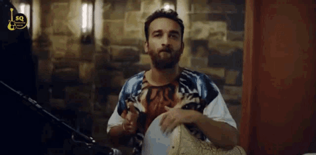 a man with a beard is playing a drum in front of a microphone with the letters sg on it