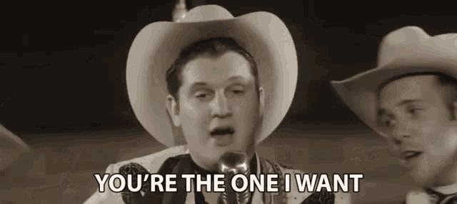 a man in a cowboy hat is singing into a microphone while another man says you 're the one i want