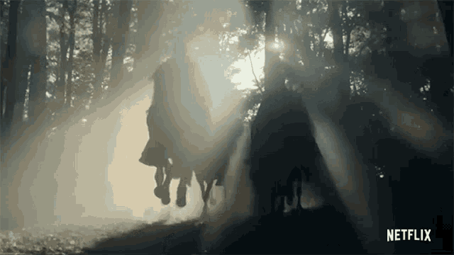 a couple of people are riding horses in the woods .