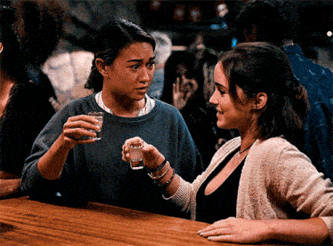 two women are sitting at a bar drinking shot glasses