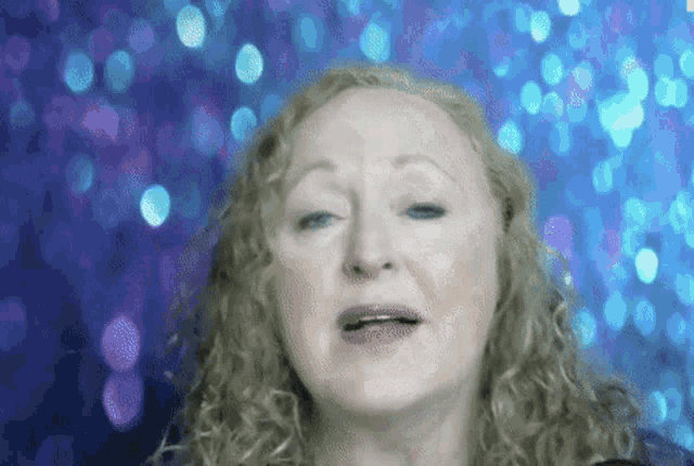 a woman with blonde curly hair is making a funny face in front of a blue background