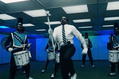 a man in a suit is dancing in front of a drum set
