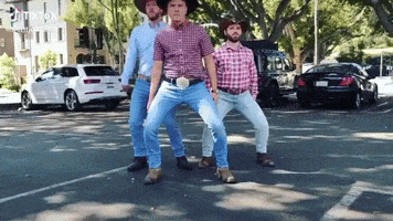 three men wearing cowboy hats and jeans are dancing in a parking lot