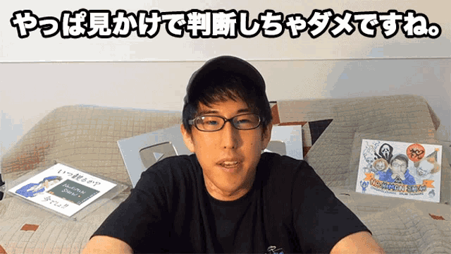 a man wearing glasses sits on a couch in front of a sign that says ' i love you ' on it